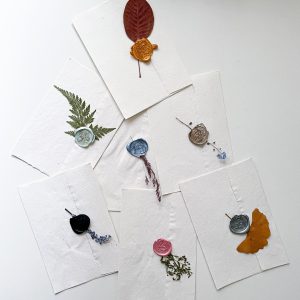 Flat lay of wax-sealed envelopes with pressed leaves offering artistic elegance on a white background.